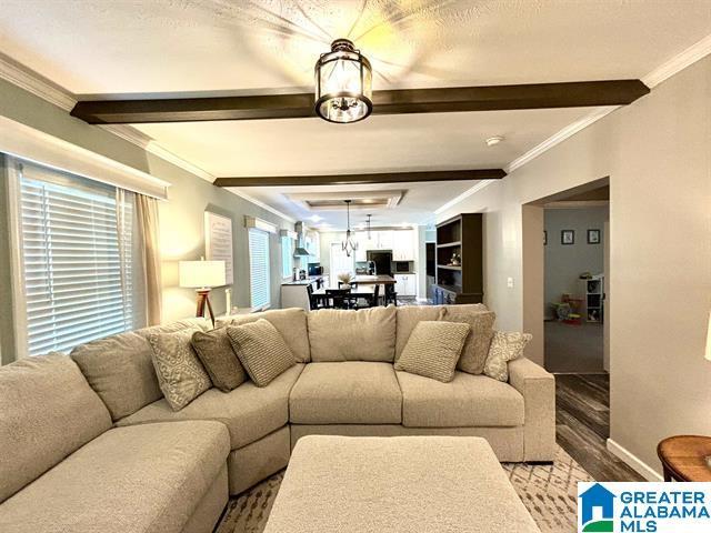 living room featuring crown molding, attic access, wood finished floors, beamed ceiling, and baseboards