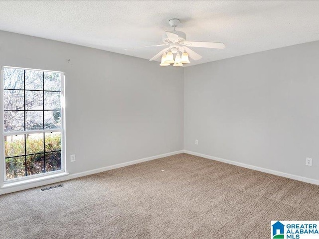 carpeted empty room featuring baseboards, ceiling fan, visible vents, and a textured ceiling