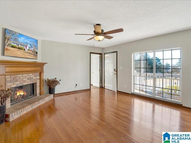 unfurnished living room featuring a textured ceiling, ceiling fan, a fireplace, wood finished floors, and baseboards