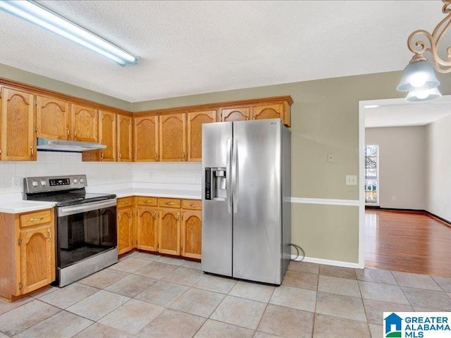 kitchen with light tile patterned floors, decorative backsplash, appliances with stainless steel finishes, light countertops, and under cabinet range hood