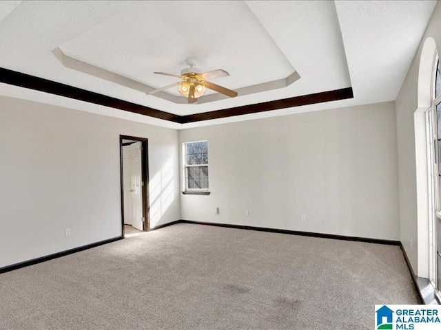 carpeted spare room featuring a ceiling fan, baseboards, a tray ceiling, and a textured ceiling