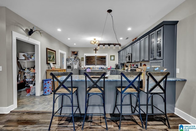 kitchen featuring appliances with stainless steel finishes, dark wood-style flooring, a peninsula, light stone countertops, and recessed lighting