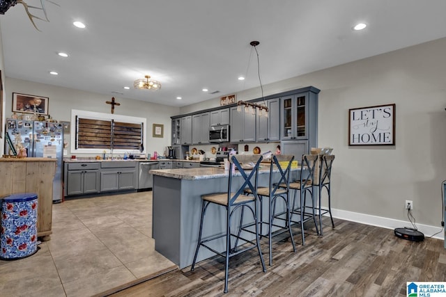 kitchen featuring gray cabinetry, stainless steel appliances, a peninsula, a kitchen breakfast bar, and glass insert cabinets