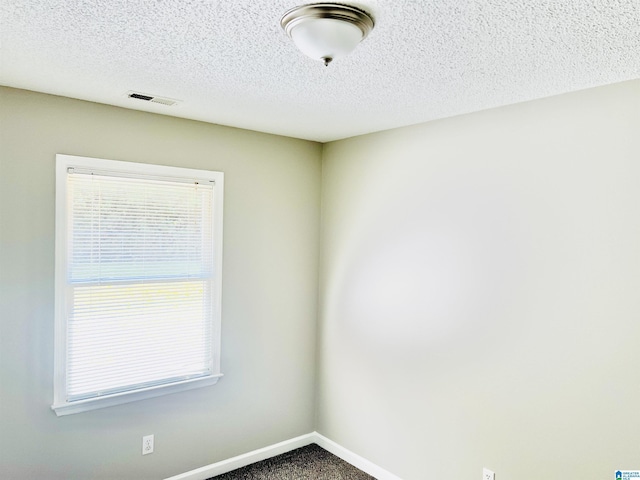 carpeted spare room featuring a textured ceiling, visible vents, and baseboards