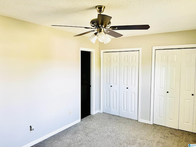 unfurnished bedroom featuring light carpet, baseboards, a ceiling fan, a textured ceiling, and multiple closets