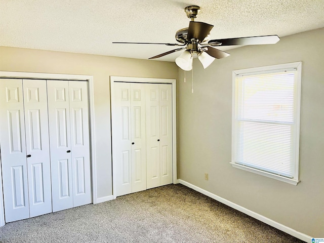 unfurnished bedroom with baseboards, a ceiling fan, a textured ceiling, carpet floors, and multiple closets