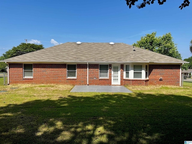 rear view of property featuring brick siding, a shingled roof, fence, a lawn, and a patio area