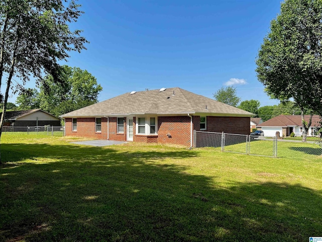 back of property with a yard, brick siding, a fenced backyard, and a gate