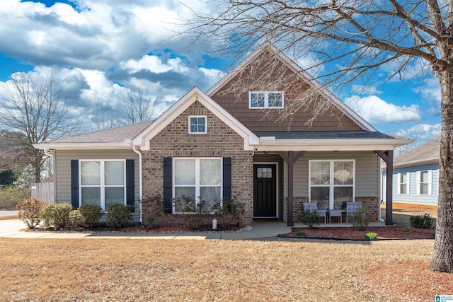 view of front of property featuring brick siding, covered porch, a front yard, and a shingled roof