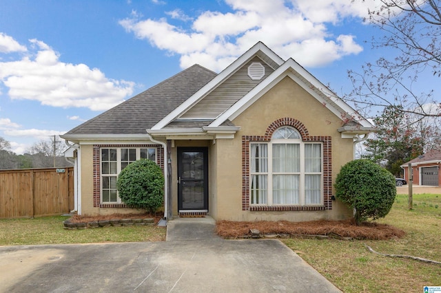 view of front of home featuring brick siding, a shingled roof, fence, a front yard, and stucco siding