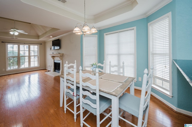 dining area featuring a fireplace with raised hearth, hardwood / wood-style floors, a raised ceiling, and ornamental molding