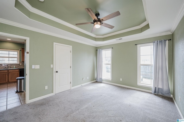 unfurnished bedroom featuring light colored carpet, a sink, visible vents, a tray ceiling, and crown molding