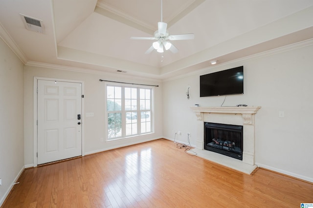 unfurnished living room featuring visible vents, a fireplace with raised hearth, a raised ceiling, ornamental molding, and wood finished floors