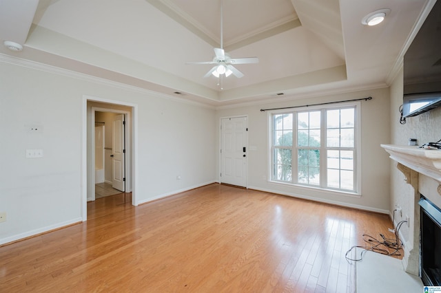 unfurnished living room featuring a high end fireplace, baseboards, light wood-style floors, ornamental molding, and a raised ceiling