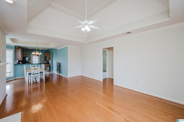 unfurnished living room featuring crown molding, a raised ceiling, visible vents, and light wood-style floors