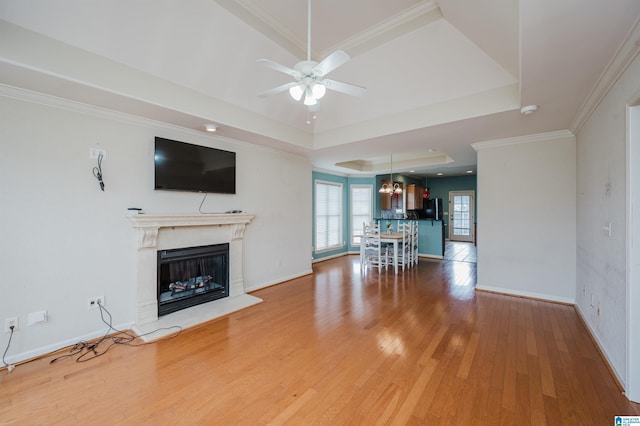 unfurnished living room with a glass covered fireplace, a raised ceiling, crown molding, and light wood finished floors