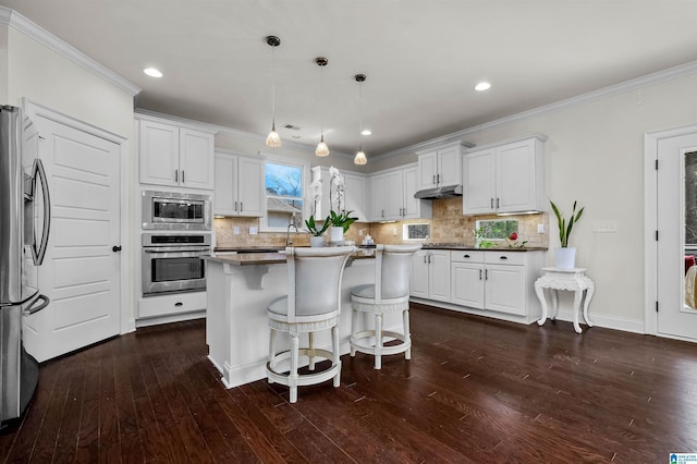 kitchen with appliances with stainless steel finishes, white cabinets, ornamental molding, and under cabinet range hood