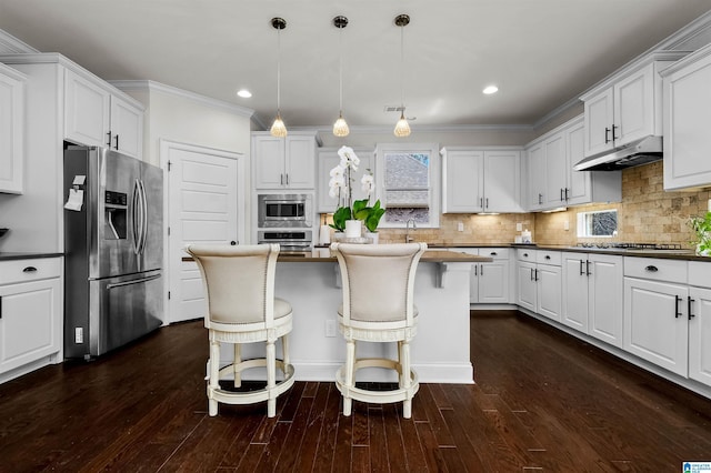 kitchen with a breakfast bar area, under cabinet range hood, stainless steel appliances, white cabinets, and backsplash