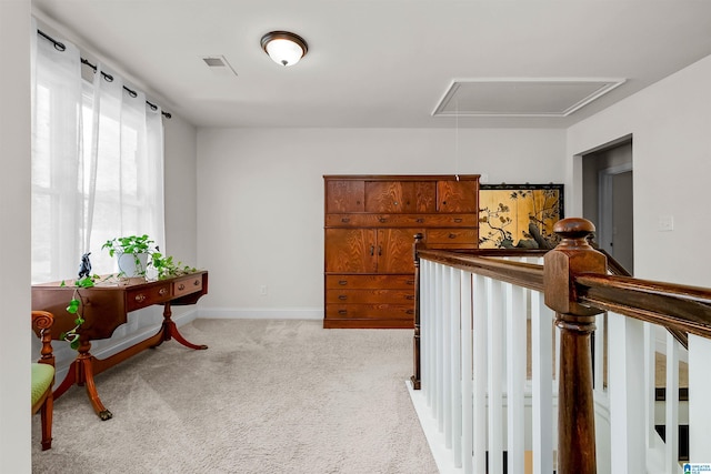 corridor featuring visible vents, baseboards, attic access, and light colored carpet