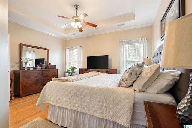 bedroom featuring a tray ceiling, visible vents, crown molding, and light wood finished floors