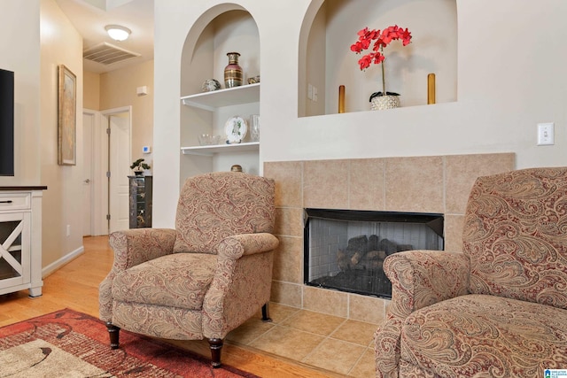 living area with built in features, a tile fireplace, visible vents, and wood finished floors