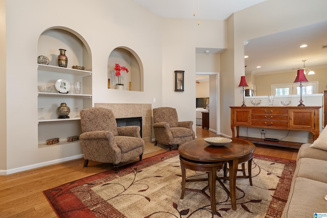 living area with built in features, recessed lighting, a tiled fireplace, wood finished floors, and baseboards