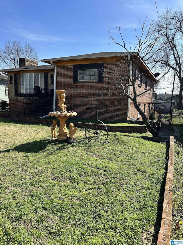 view of front of house with a front yard, crawl space, brick siding, and a chimney