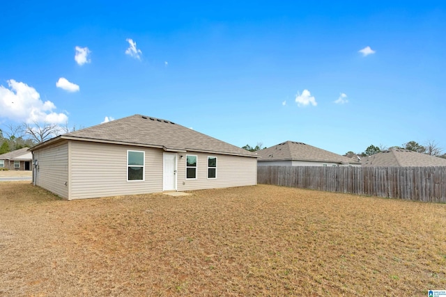 back of house featuring a shingled roof, a lawn, and fence