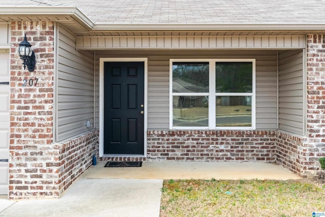 entrance to property featuring a garage, brick siding, and roof with shingles