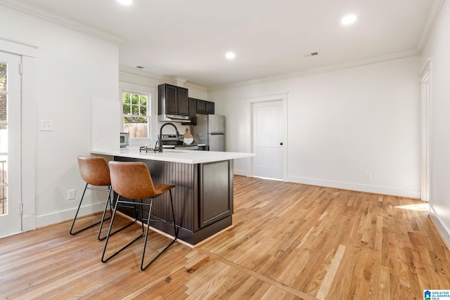 kitchen featuring a breakfast bar, light countertops, freestanding refrigerator, and ornamental molding