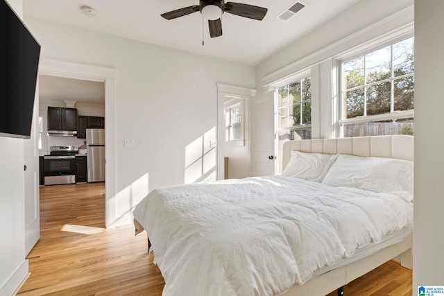 bedroom featuring light wood finished floors, visible vents, freestanding refrigerator, and a ceiling fan