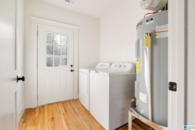 washroom with visible vents, washing machine and clothes dryer, laundry area, light wood-style flooring, and water heater