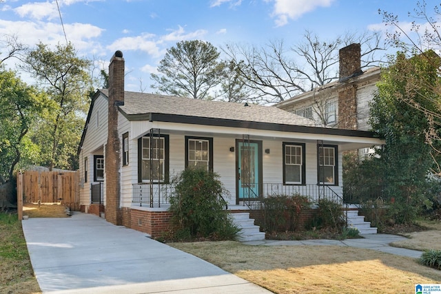 view of front of home with a porch, concrete driveway, fence, and a chimney