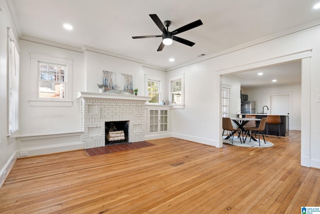 living area with ceiling fan, a fireplace, wood-type flooring, and ornamental molding