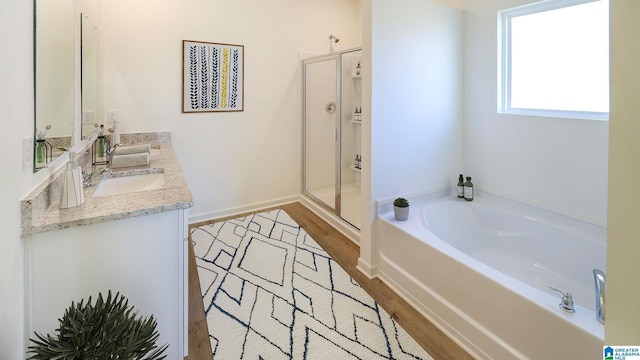 bathroom featuring a garden tub, a sink, wood finished floors, double vanity, and a stall shower