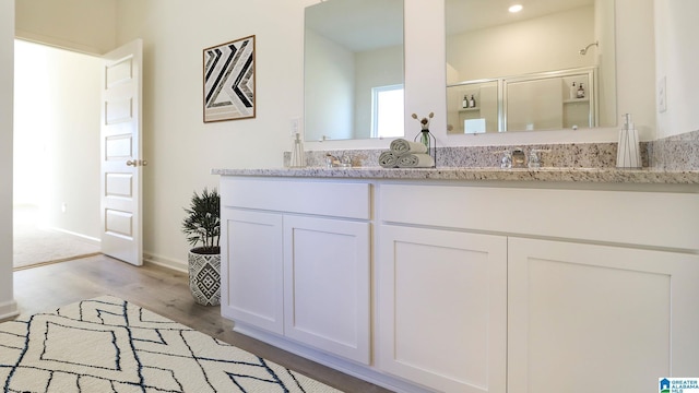 bathroom with double vanity, recessed lighting, a shower with shower door, a sink, and wood finished floors