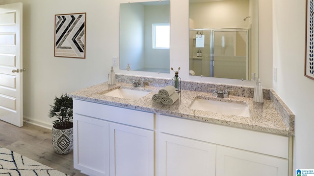 bathroom featuring double vanity, a stall shower, a sink, and wood finished floors