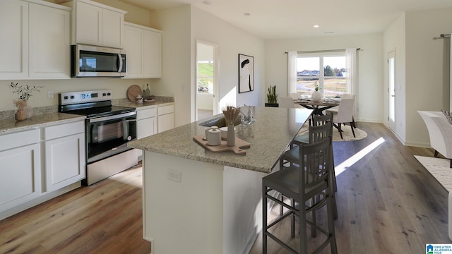 kitchen with light stone counters, a sink, white cabinets, light wood-style floors, and appliances with stainless steel finishes