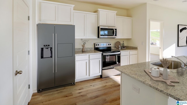 kitchen featuring light stone counters, light wood-style flooring, stainless steel appliances, a sink, and white cabinets