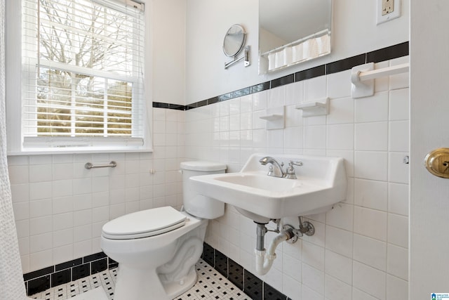 bathroom featuring tile patterned floors, toilet, tile walls, and a sink