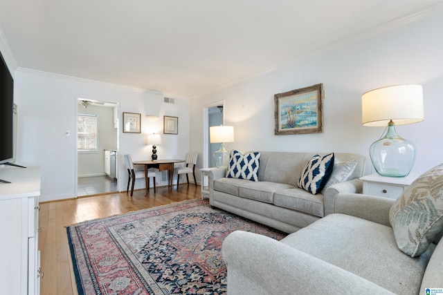 living area featuring visible vents, light wood-type flooring, baseboards, and ornamental molding