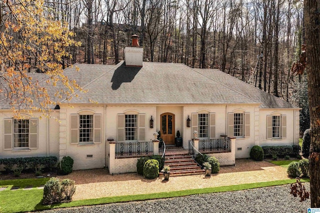 view of front of home with covered porch, brick siding, roof with shingles, crawl space, and a chimney