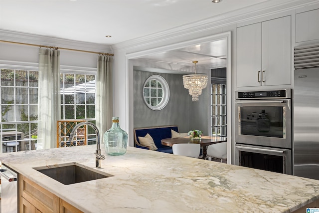 kitchen featuring a notable chandelier, appliances with stainless steel finishes, ornamental molding, a sink, and light stone countertops