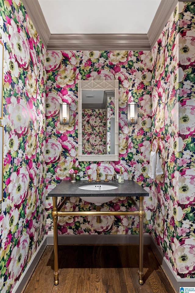 bathroom with wallpapered walls, wood finished floors, a sink, and crown molding