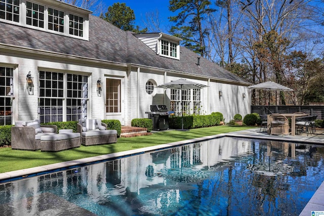 rear view of property with a shingled roof, brick siding, an outdoor pool, and a patio