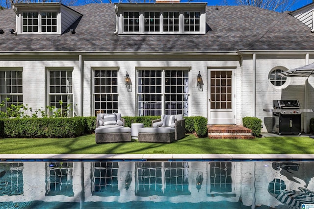 rear view of house with brick siding, a shingled roof, a lawn, an outdoor hangout area, and an outdoor pool