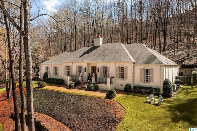 view of front of home featuring a porch, a front lawn, a chimney, and a shingled roof