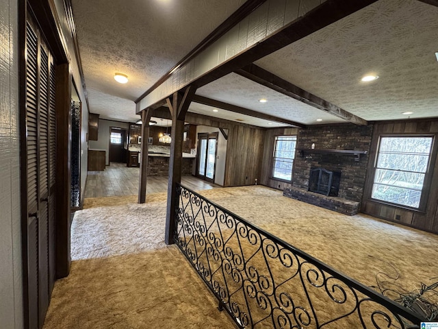 corridor with carpet, beam ceiling, wood walls, and a textured ceiling