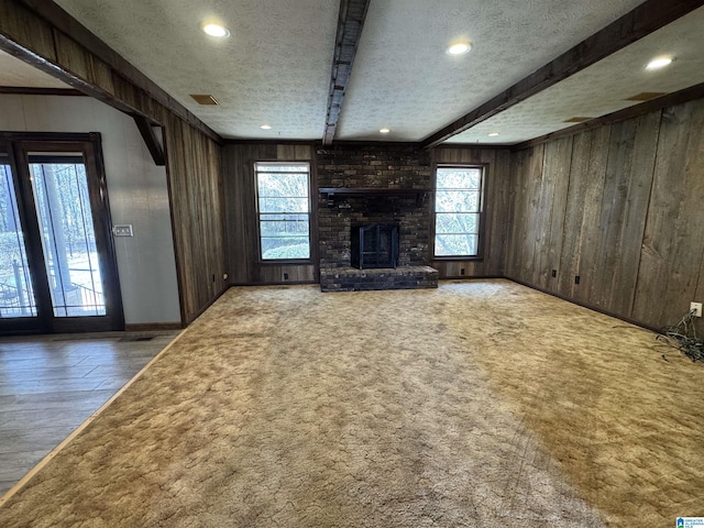 unfurnished living room with beamed ceiling, carpet, a textured ceiling, wood walls, and a fireplace