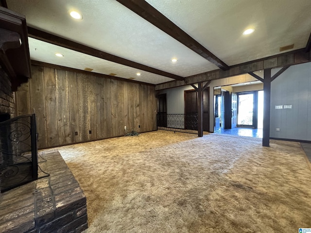 unfurnished living room with wooden walls, carpet, a fireplace, and beamed ceiling